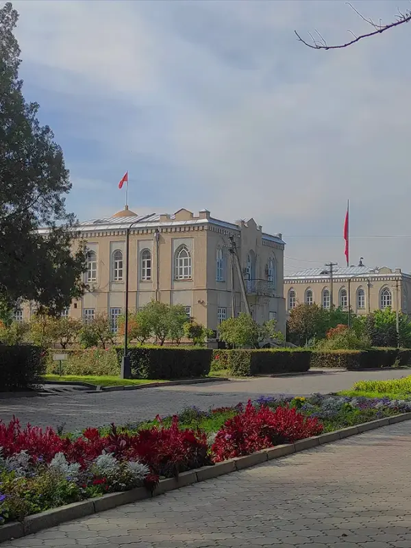 Цветочные клумбы, деревья и историческое здание в центре Бишкека