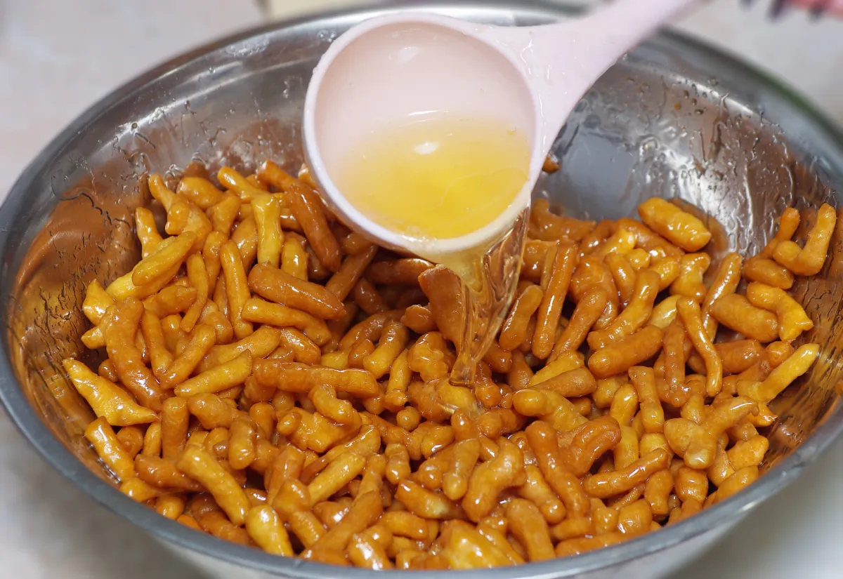 Sirop de miel chaud versé sur les morceaux de pâte frits