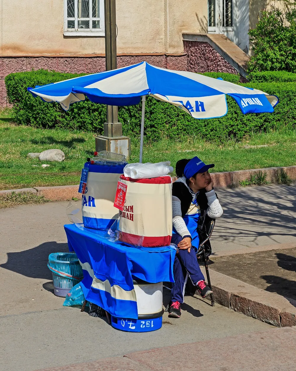 Vendeur devant deux cuves isothermes de tan et de maksym sous un parasol dans une rue de Bichkek
