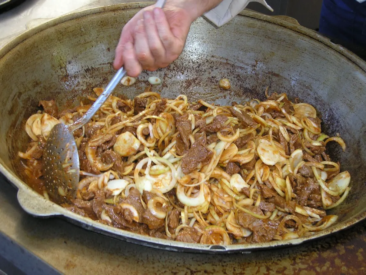 Viande et grande quantité d’oignons en cours de cuisson dans un large chaudron