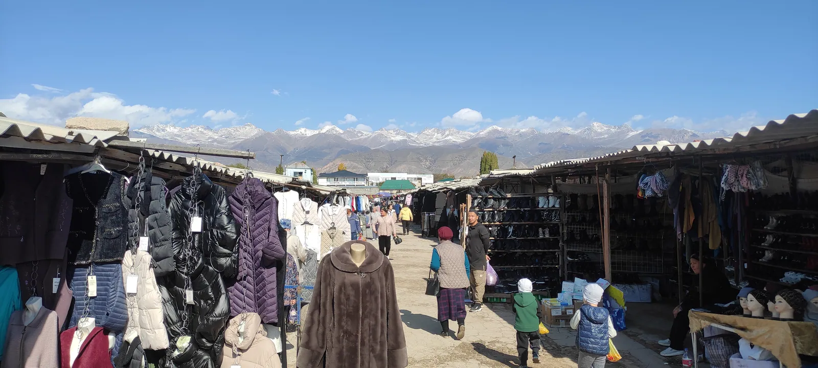 Allée de vêtements et de chaussures du marché de Bosteri avec les montagnes enneigées à l’arrière-plan