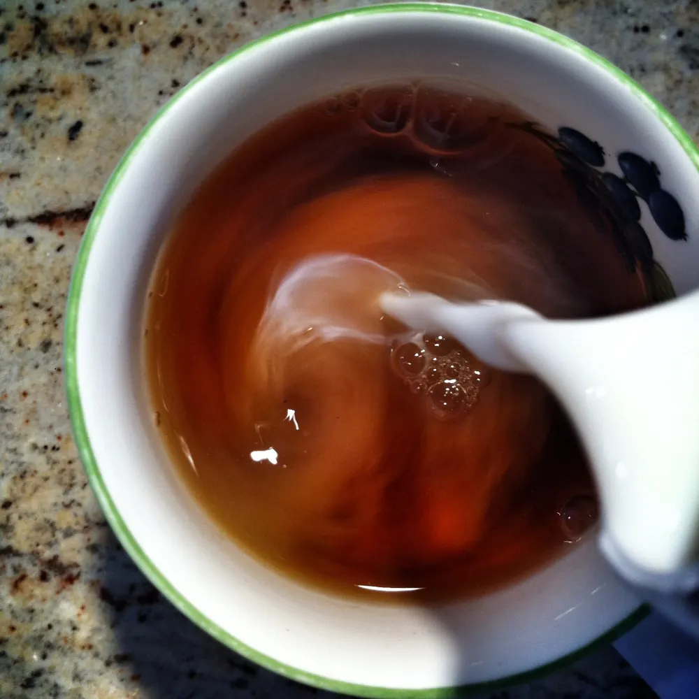 Du lait versé dans une tasse de thé noir Assam, avec des volutes claires