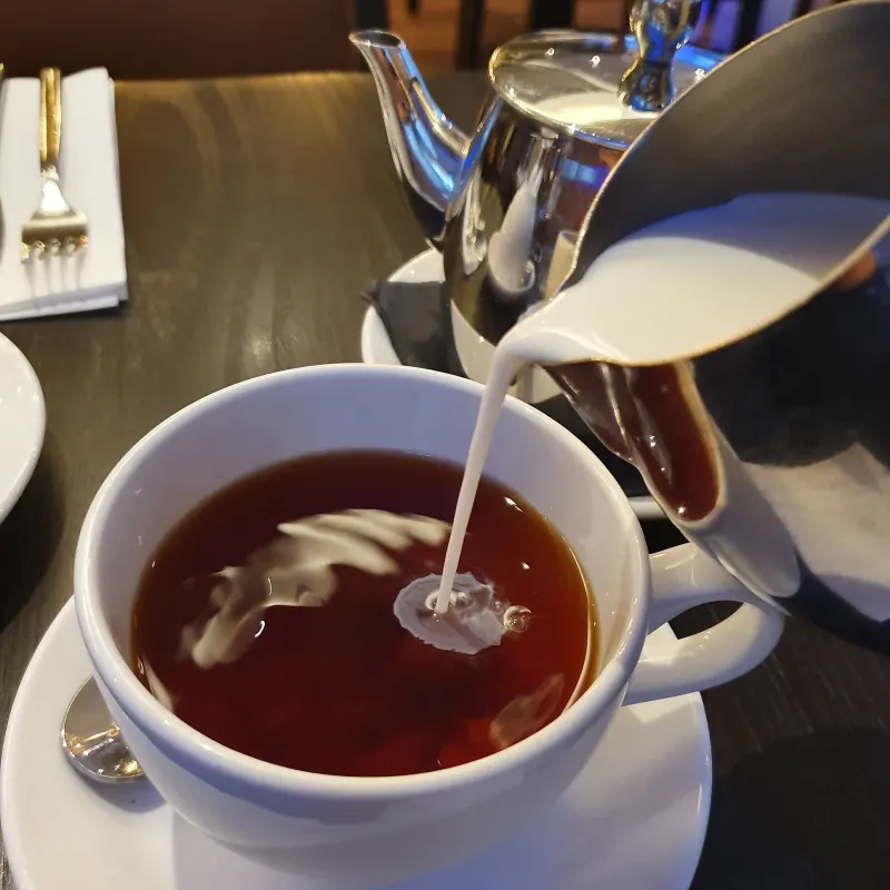 Du lait versé dans une tasse de thé noir corsé
